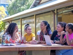 A group of people having a meeting outside with a laptop.