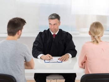 Two people at a table in front of a lawyer or judge. 