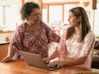 Two women working on a laptop together in a kitchen. 