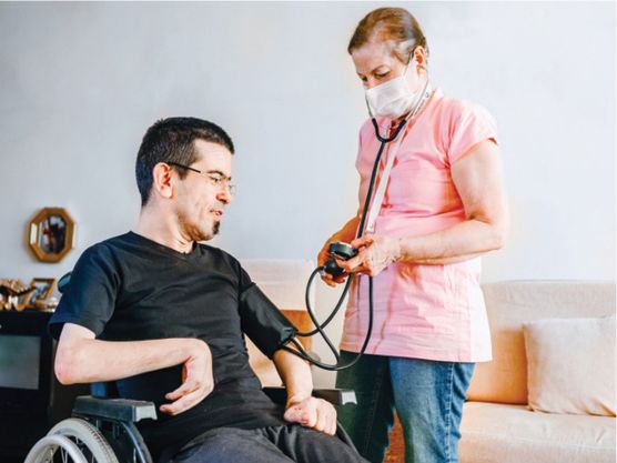 A carer supporting a person. The carer is checking the blood pressure of the person they are supporting.