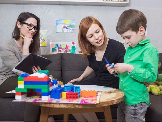 A child with disability being supported by a teacher and their parent.