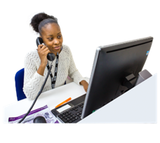 A person at a computer, talking on the phone.