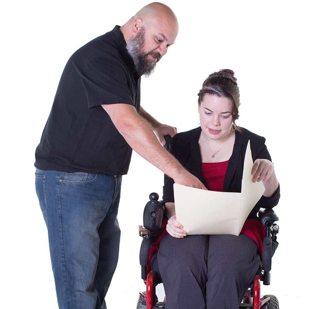 A person supporting someone is a wheelchair to read a document.