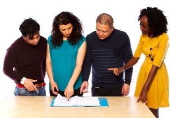 A group of people standing around a a table reading a document.
