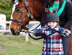 A photo of a child wearing a horse riding helmet next to a horse.